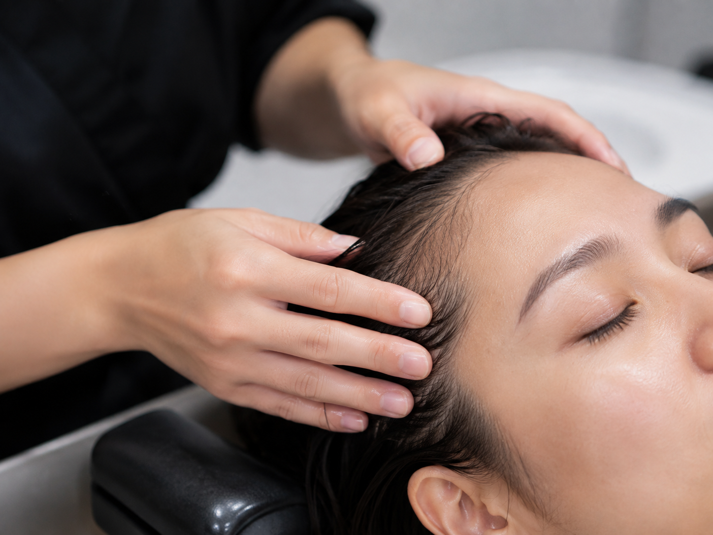 Practitioner uses light fingertip contact and minimal product at the client's hairline during a low-stimulation service adjustment.